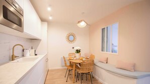 A modern kitchen with white cabinets, a built-in oven, and a dining area with a round table and wicker chairs. - Résidence Saint-Tropez FENIERS (Saint-Tropez)