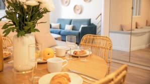 A breakfast setting with a wicker chair, a wooden table, a vase with flowers, and a blue sofa in the background. - Résidence Saint-Tropez FENIERS (Saint-Tropez)