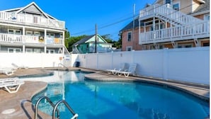 A swimming pool with lounge chairs, a white fence, and a multi-story building with balconies. - Harbor Breeze 53 by Seaside Vacations & Sales (Ocean City)
