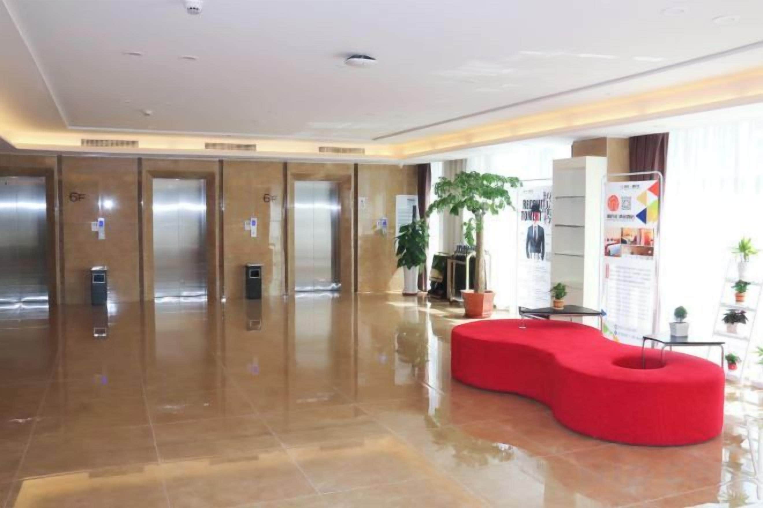 A hotel lobby with elevators, a red seating area, and a reception desk.