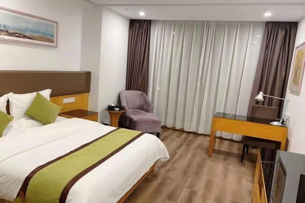 Ein Hotelzimmer mit einem Bett, einem Schreibtisch, einem Sessel, einem Fernseher und Vorhängen.