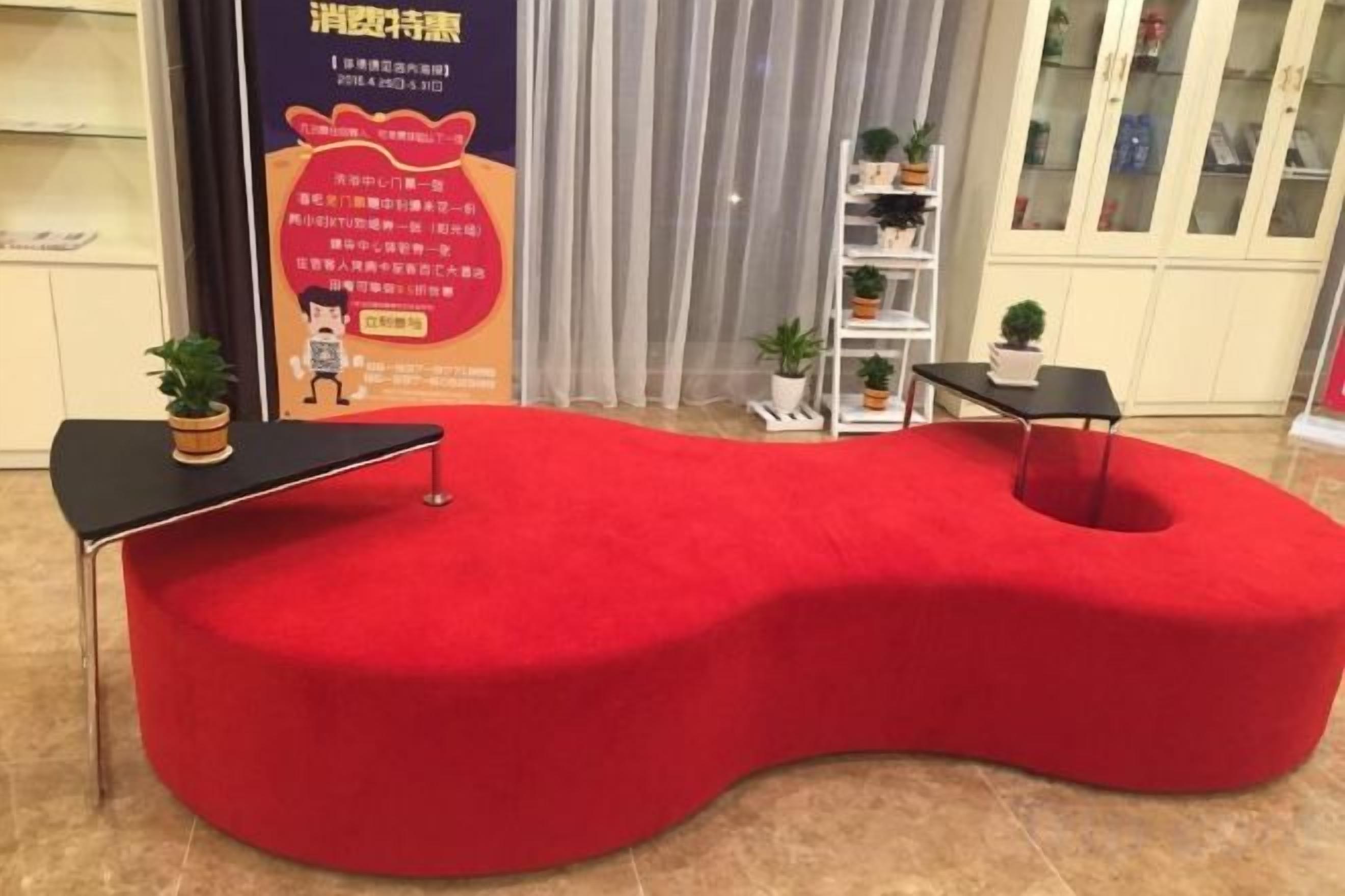 A red, curved reception desk with a small table and a potted plant.