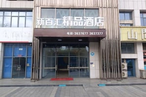 A hotel entrance with a glass facade, a red carpet, and a signboard with contact numbers. - New Baihui Boutique Hotel (Jining)