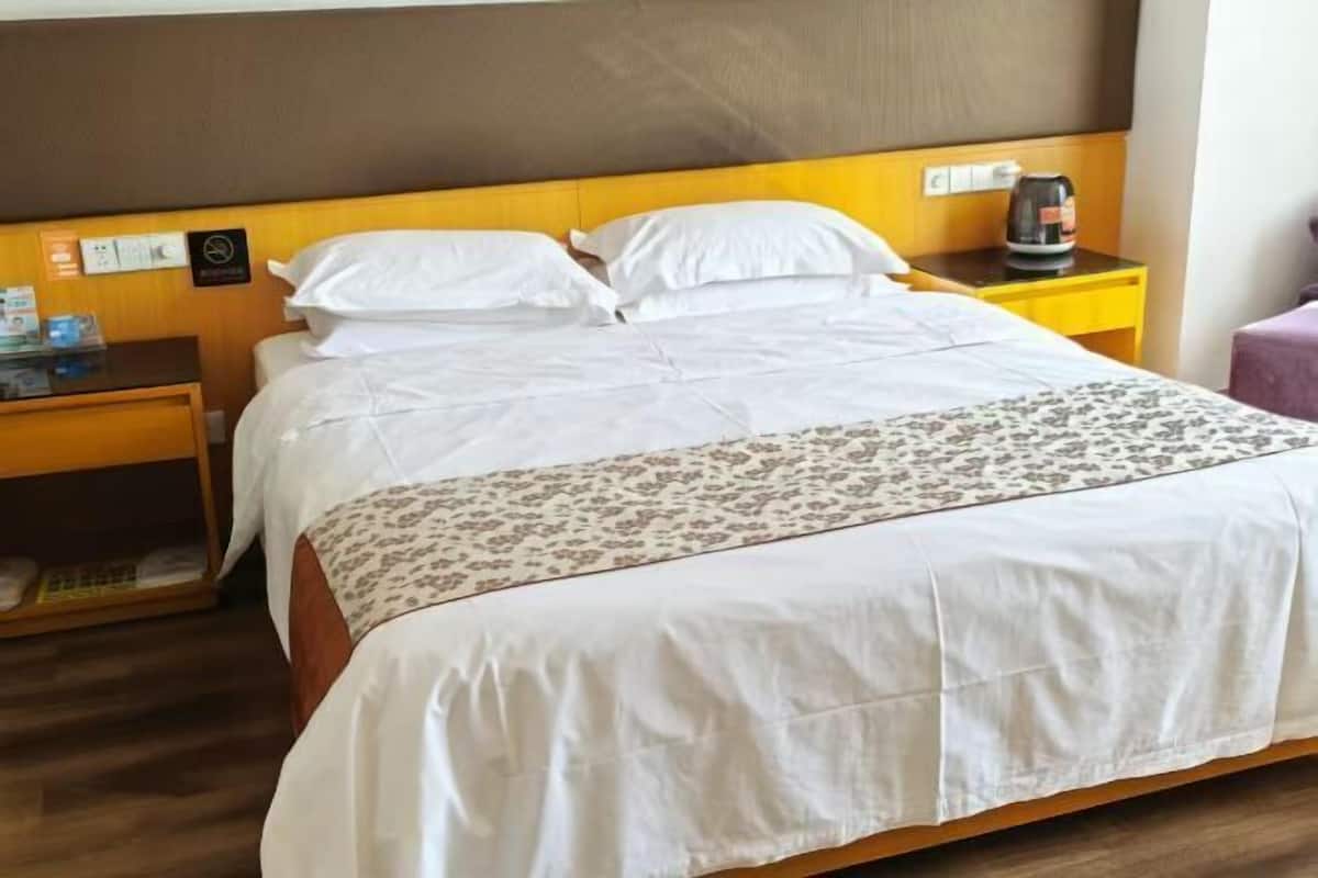 Ein Hotelzimmer mit Bett, Nachttisch, Kaffeemaschine und einem kleinen Tisch mit violettem Stuhl.