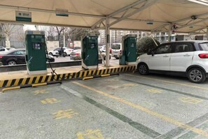 Un área de estacionamiento techada con espacios delimitados, un coche blanco aparcado y una barrera verde y amarilla.