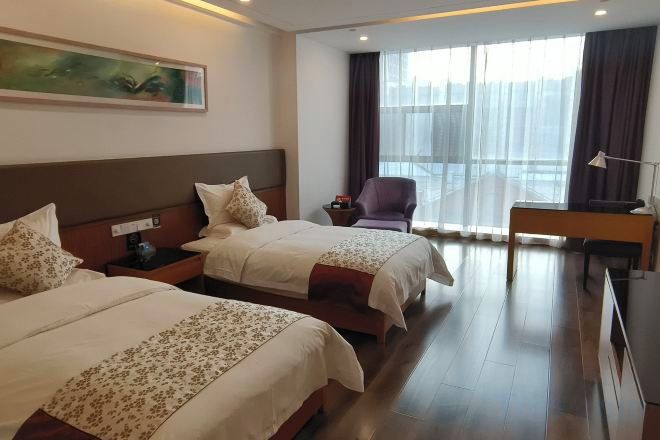 A hotel room with two beds, a desk, a chair, and a large window with curtains.