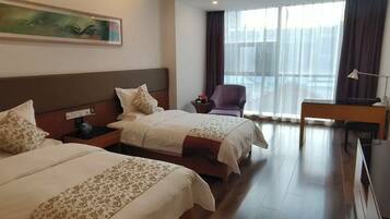 A hotel room with two beds, a desk, a chair, and a large window with curtains.