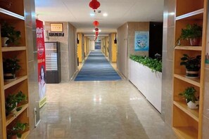 Pasillo de hotel con alfombra azul, plantas en macetas y señalizaciones en las paredes.