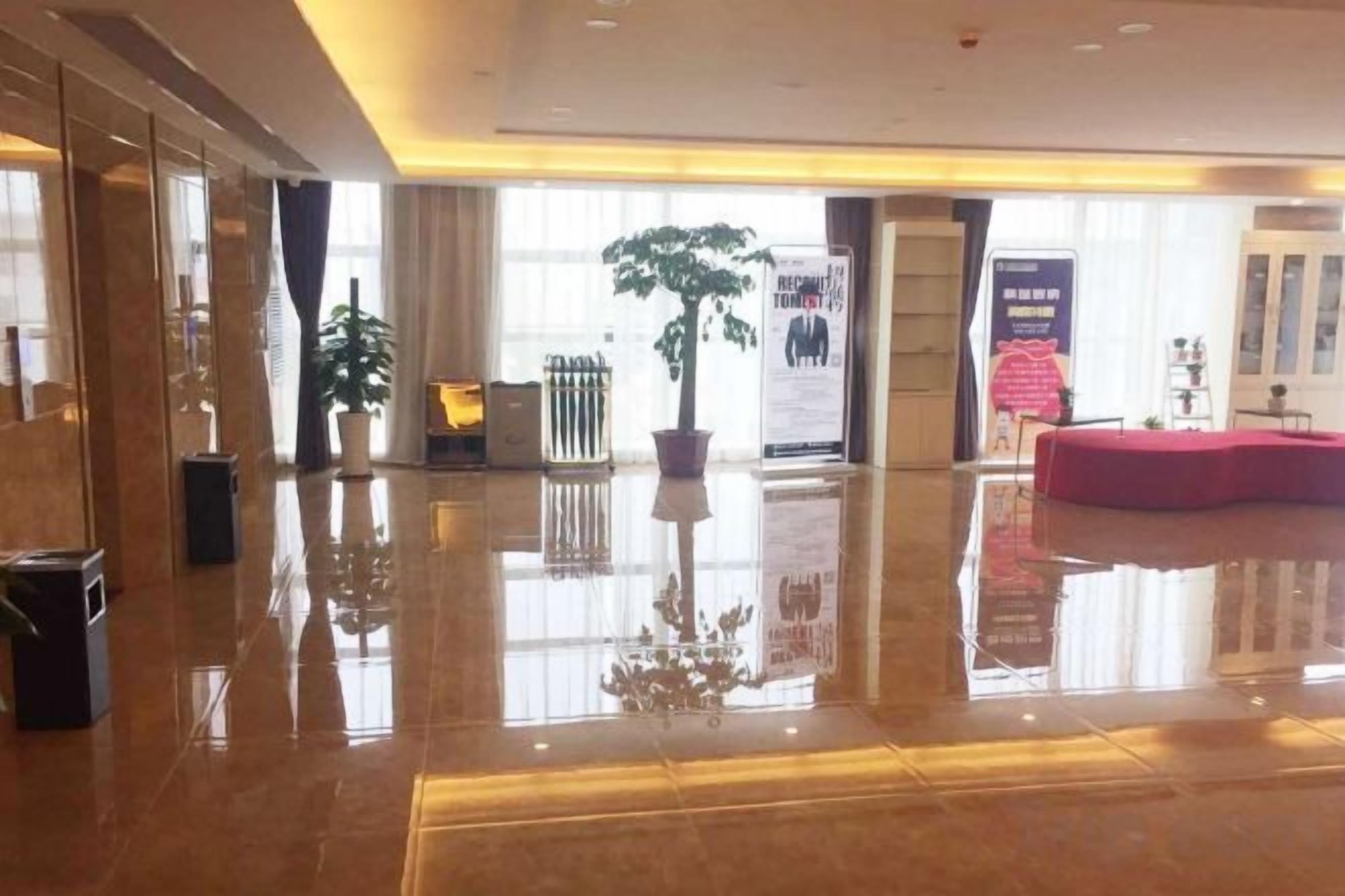 A spacious lobby with a polished floor, potted plants, and a red seating area.