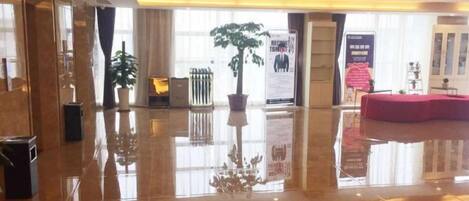 A spacious lobby with a polished floor, potted plants, and a red seating area.