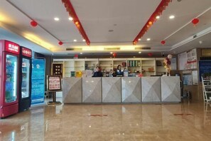 A hotel reception area with a marble counter, a red beverage machine, and a blue information board. - New Baihui Boutique Hotel (Jining)