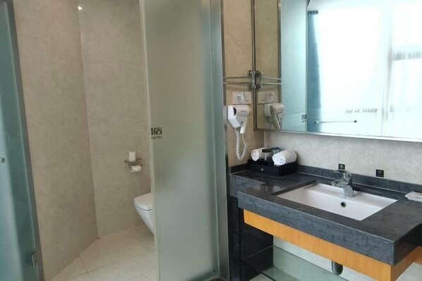 A modern bathroom with a glass shower enclosure, a sink with a dark countertop, and a mirror above the sink. - New Baihui Boutique Hotel (Jining)