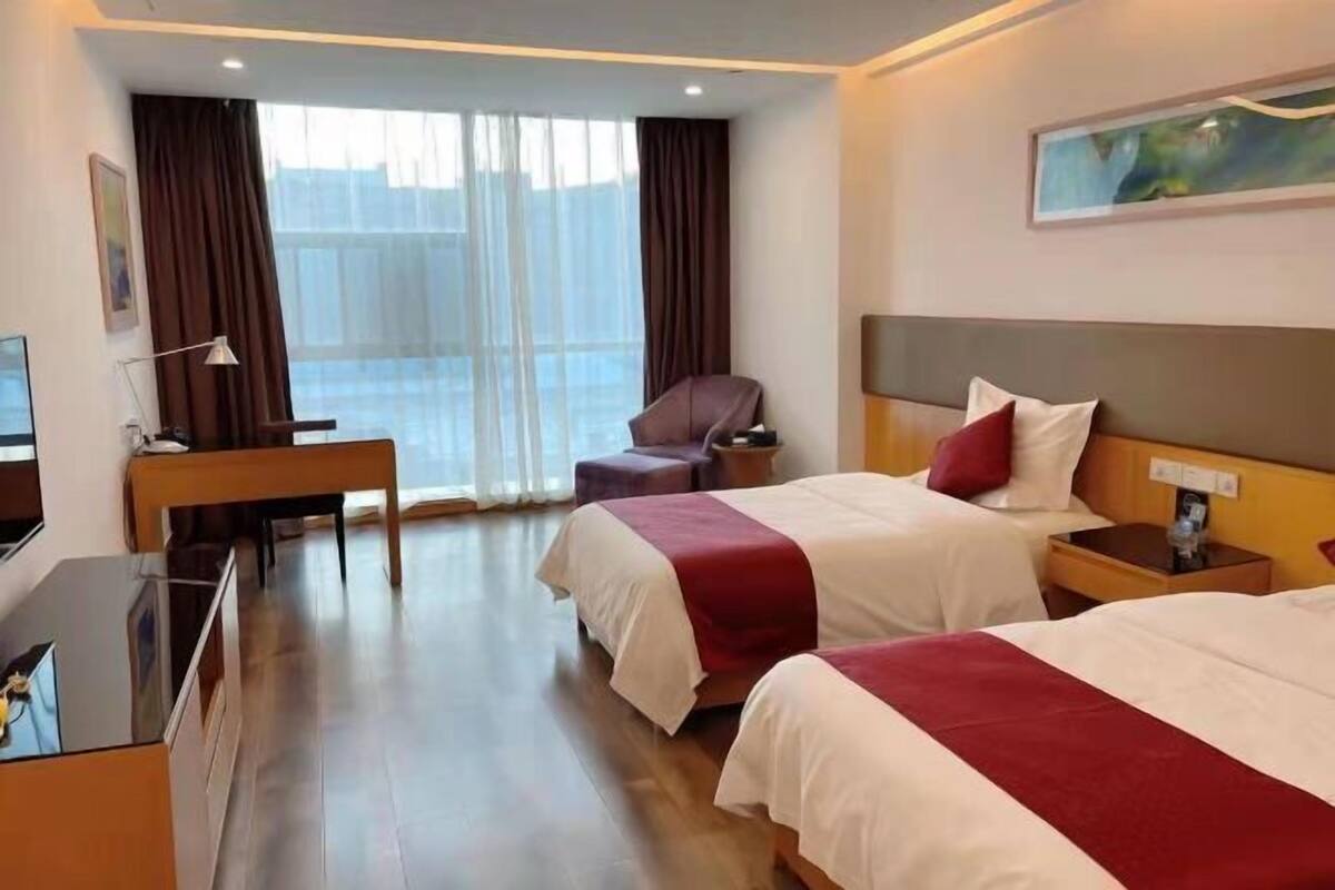 Ein Hotelzimmer mit zwei Betten, einem Schreibtisch, einem Stuhl und einem großen Fenster mit Vorhängen.
