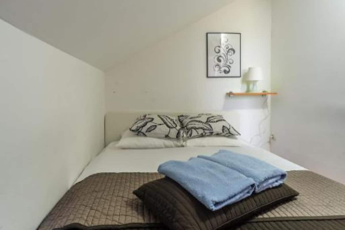 A single bed with a patterned pillow, a folded towel, and a wall-mounted picture.