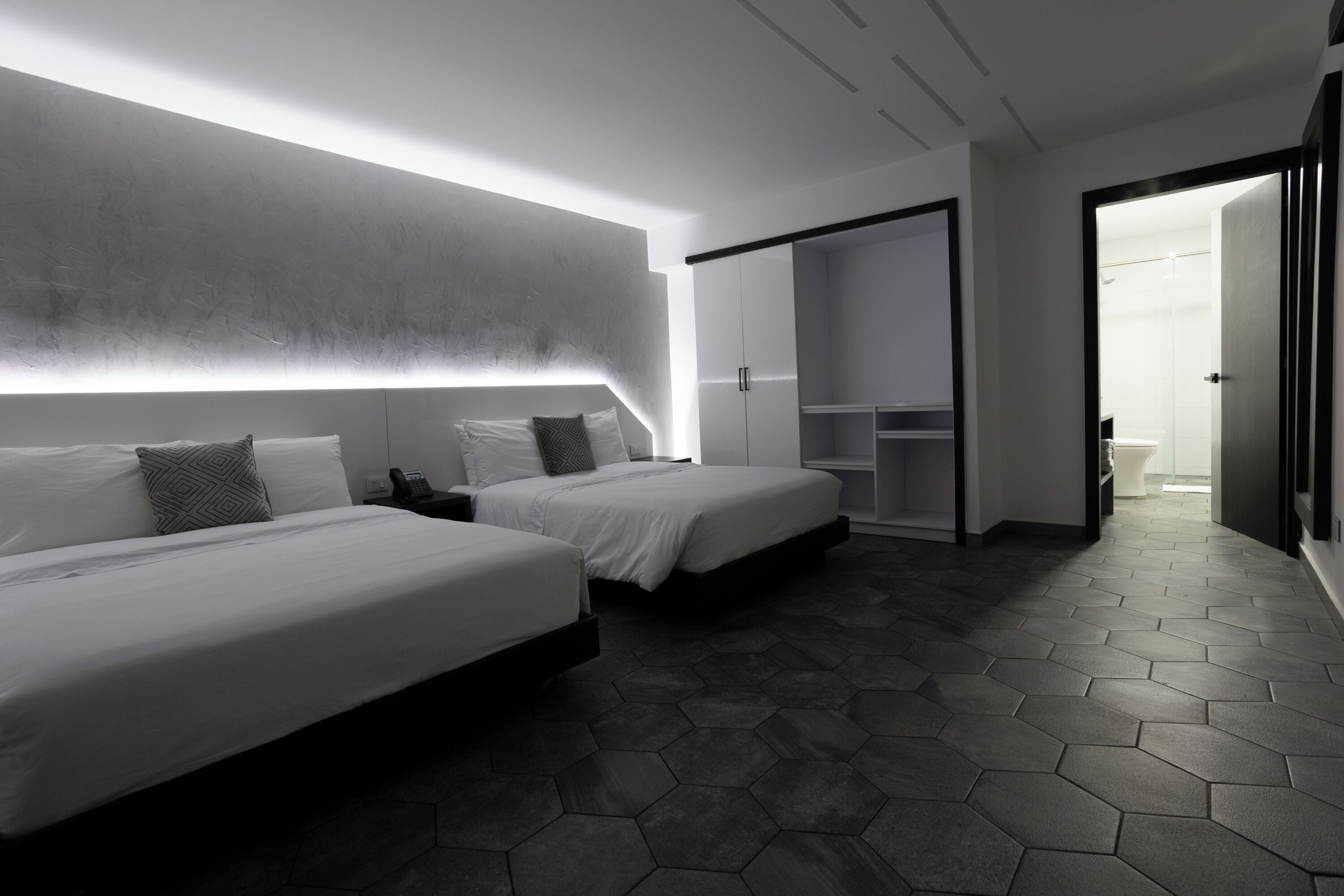 A modern hotel room with two beds, a wardrobe, and a bathroom visible through an open door.