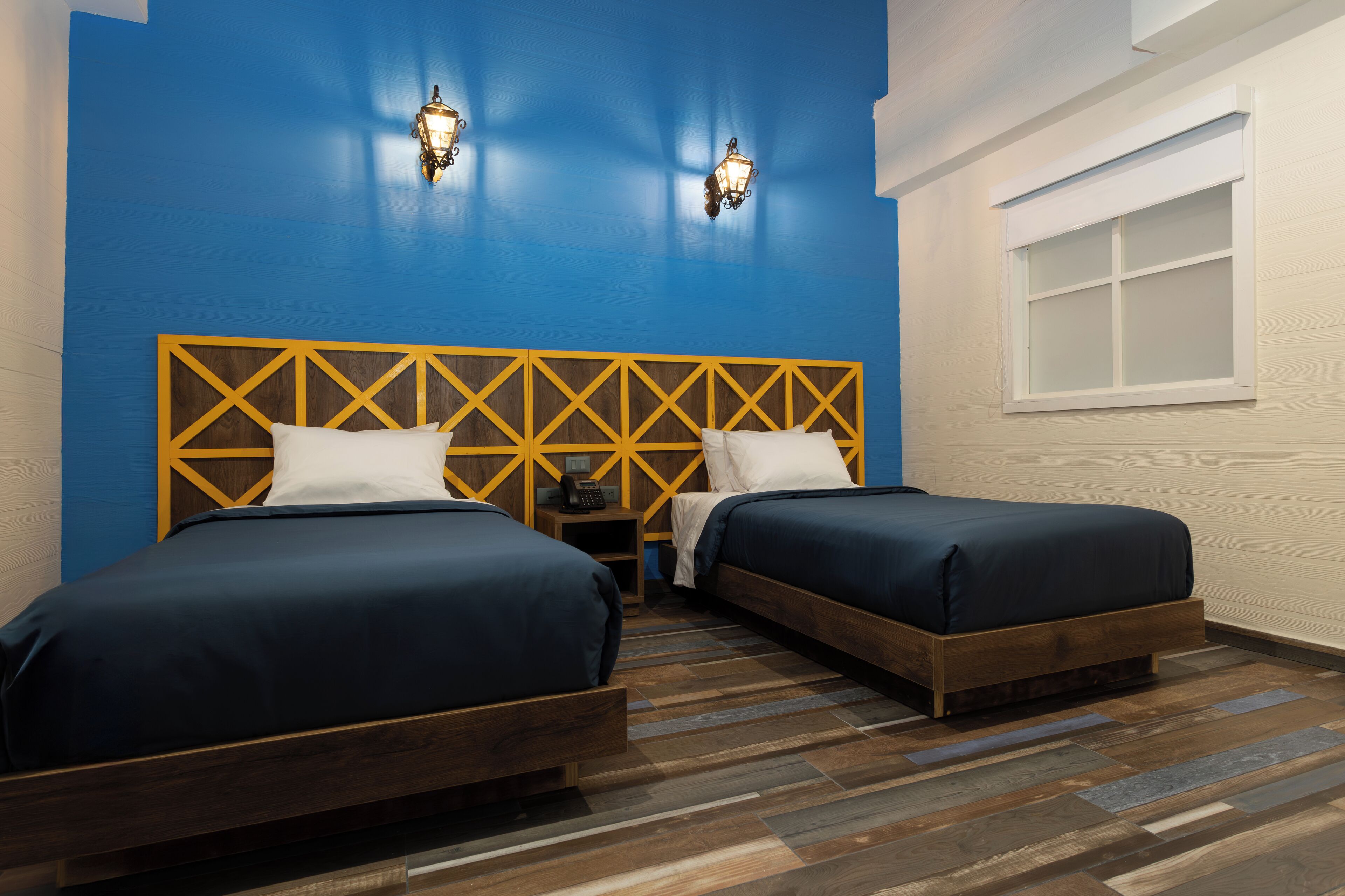 Une chambre avec deux lits, une tête de lit en bois et une fenêtre.