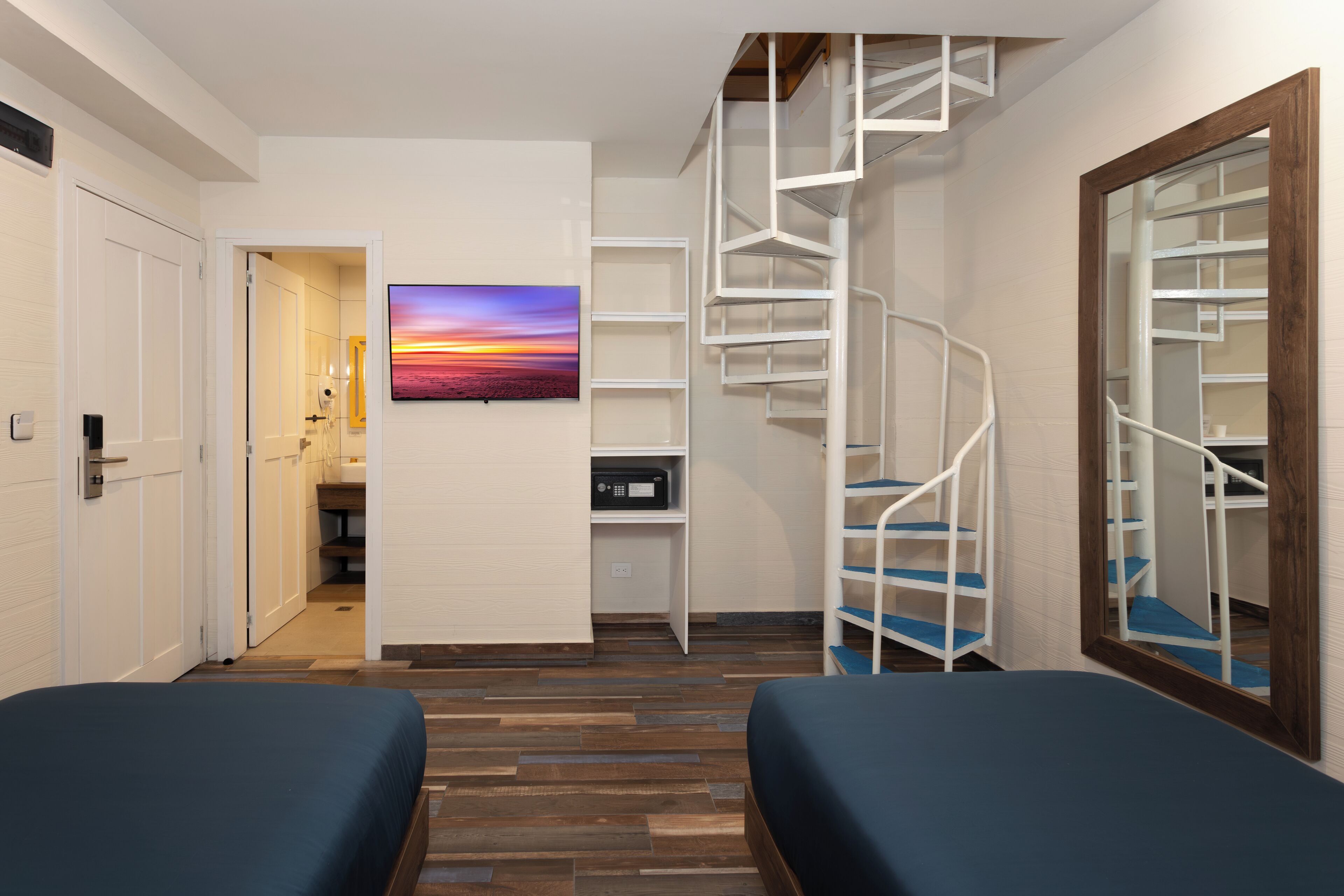 Une chambre avec un plancher en bois, un lit, un escalier en colimaçon blanc et un tableau représentant un coucher de soleil.