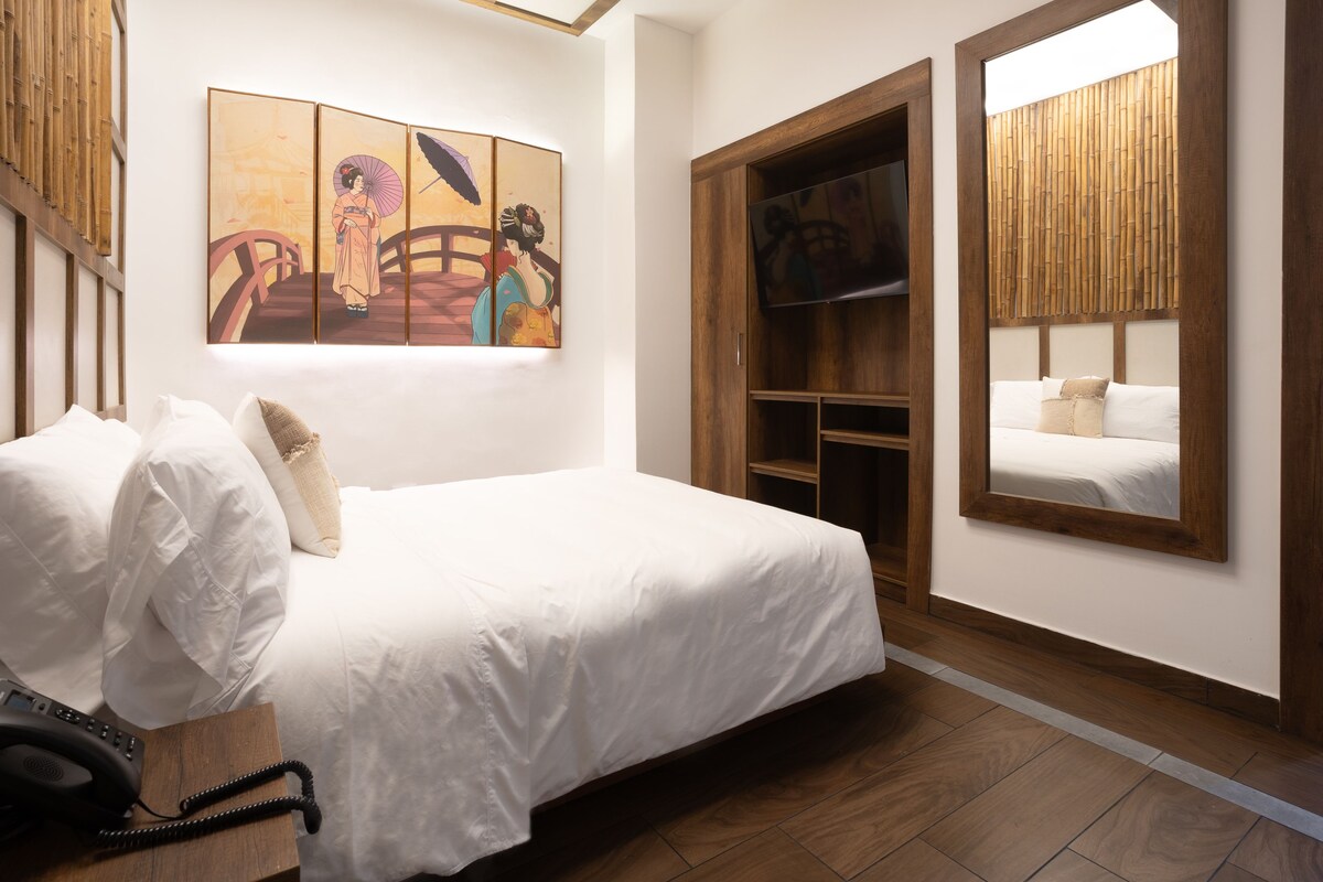 A bedroom with a bed, a wooden wardrobe, a television, and a painting on the wall.