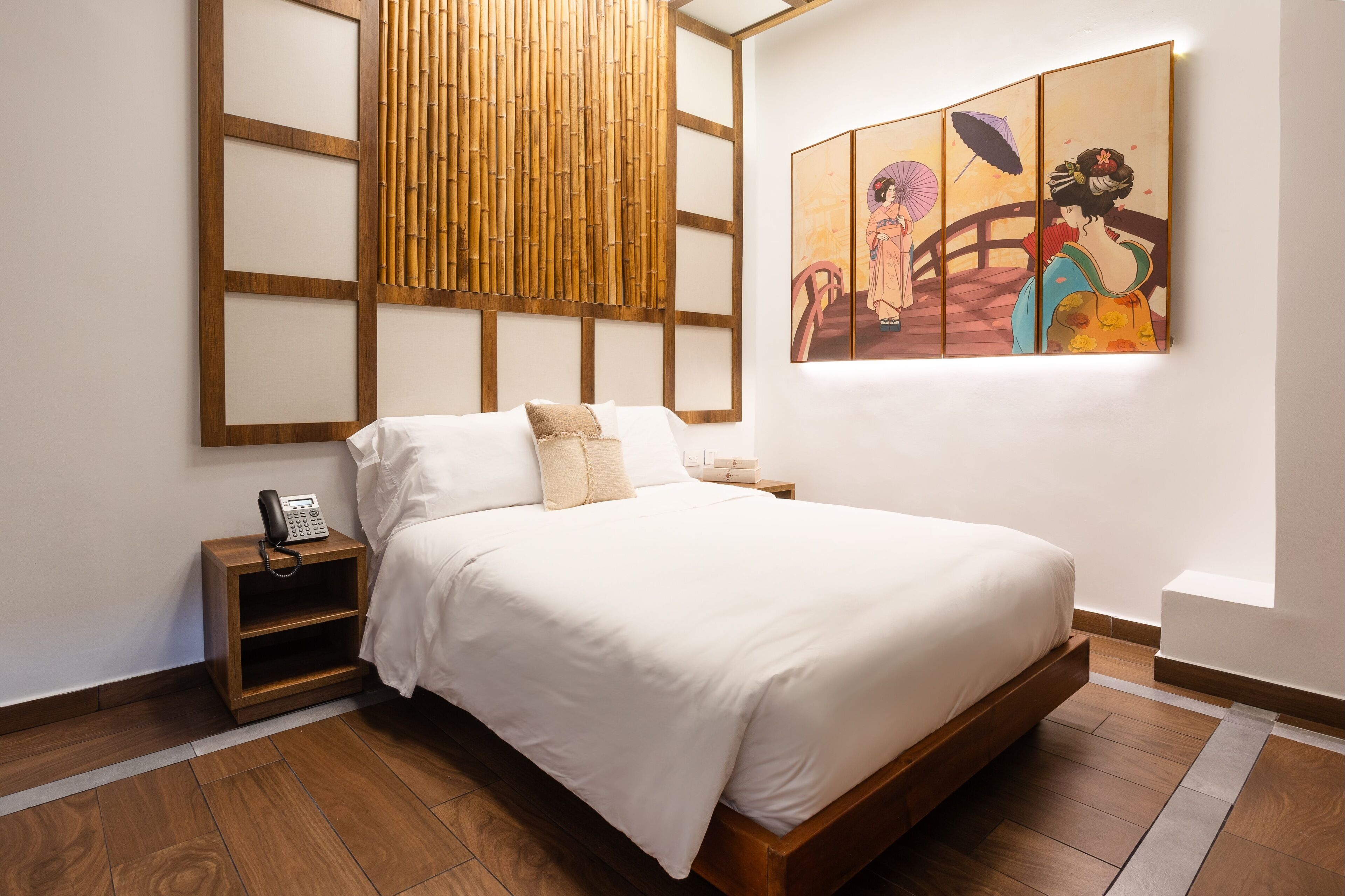 Een moderne hotelkamer met een groot bed, een houten hoofdeinde, een nachtkastje met een telefoon en een kunstwerk aan de muur.