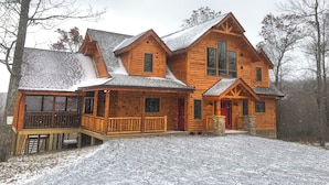 Eine große Holzhütte mit Veranda und mehreren Fenstern, umgeben von Bäumen und bedeckt mit Schnee.