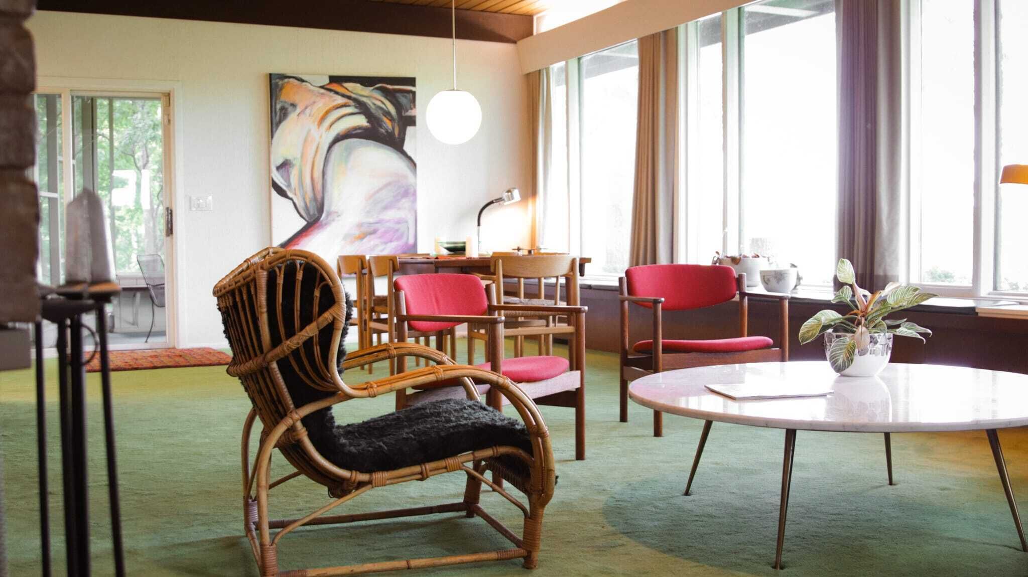 A room with a round table, wicker chairs, and a large abstract painting on the wall.