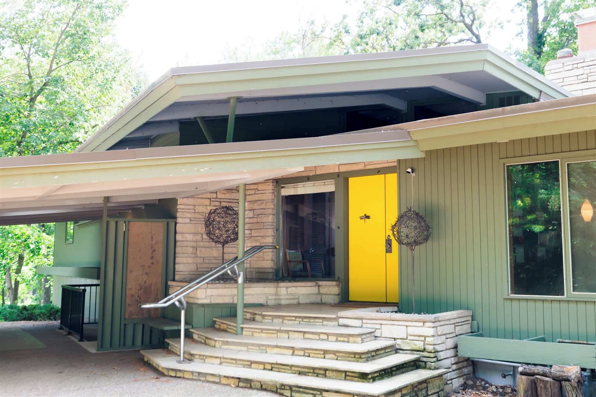 A two-story house with a yellow front door, a covered porch, and a staircase leading to the entrance.