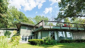 Une maison à deux étages dotée d’un balcon, entourée d’une végétation luxuriante et d’arbres.