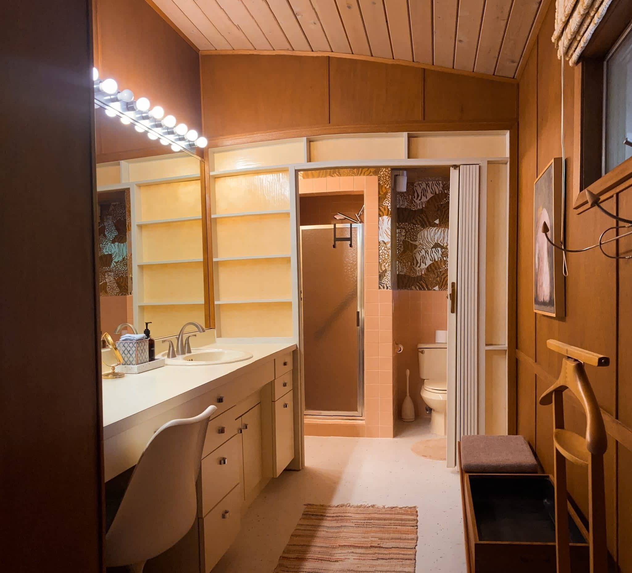 Une salle de bain moderne avec un meuble-lavabo, un évier et un miroir. On aperçoit un espace douche à travers une porte ouverte.