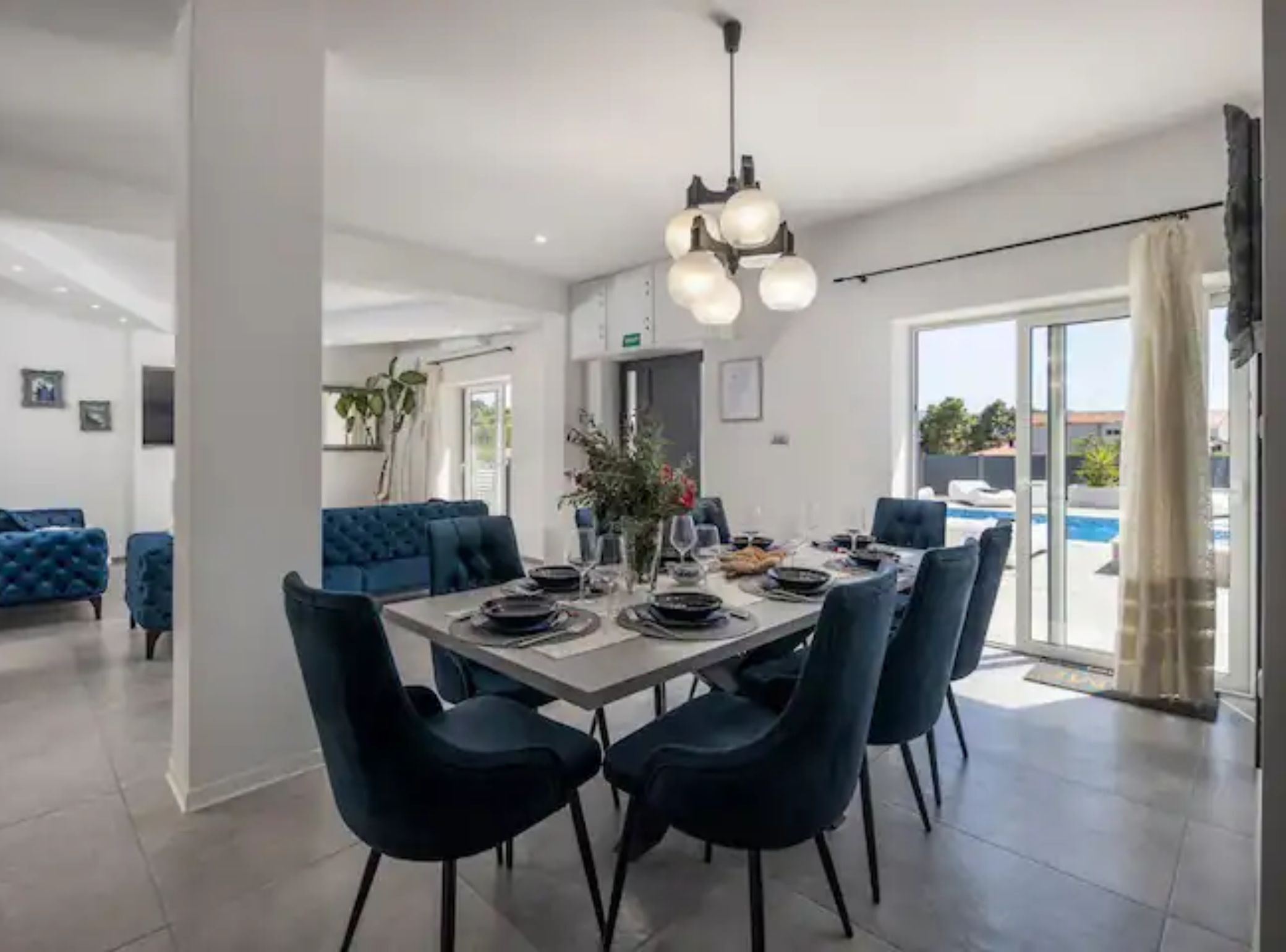A modern dining area with a large table set for six, surrounded by dark blue chairs.