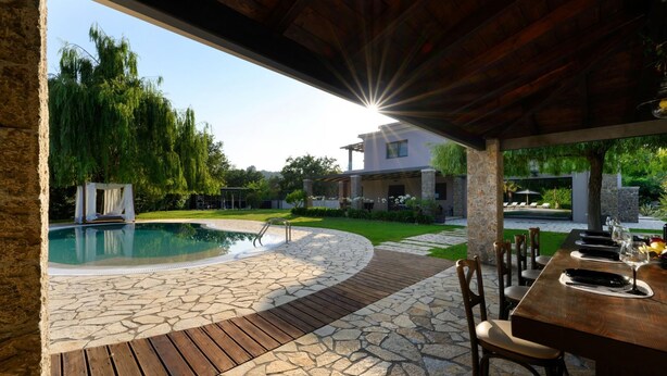 Un espace piscine doté d’une terrasse en pierre, d’une terrasse en bois et d’un coin salon couvert avec une table et des chaises.