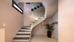 Un escalier moderne avec des rampes en verre et un design incurvé, menant à un palier agrémenté d’éléments décoratifs et d’une plante en pot.