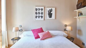 A neatly made bed with white linens and two pillows, a bedside table with a lamp, and a wall with two framed cactus artworks. - Eusebio Planas  - Two Bedroom Apartment, Sleeps 4 (Barcelona)