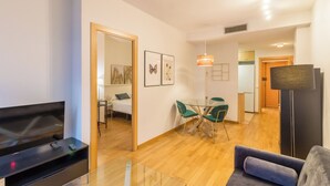 Una sala de estar moderna con un televisor de pantalla plana, una mesa de centro de vidrio, un sofá y un comedor con mesa y sillas.