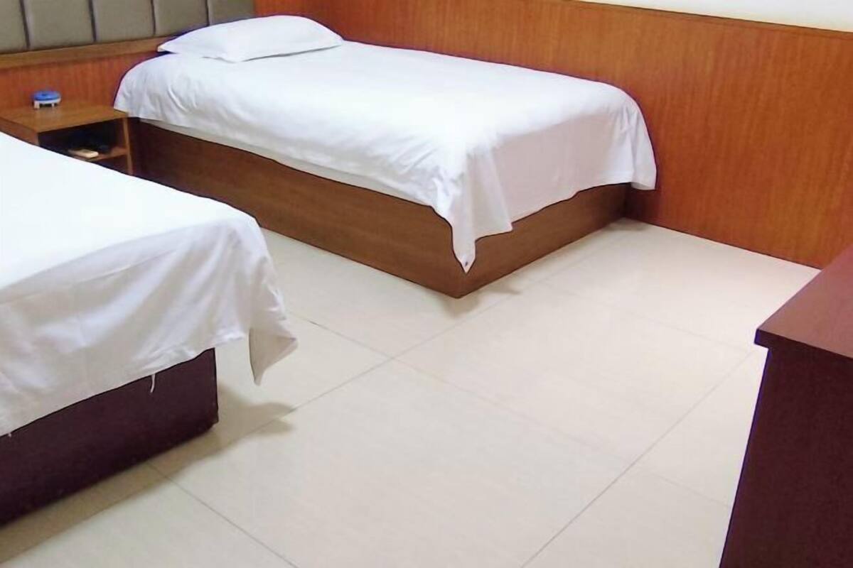 Een kamer met twee eenpersoonsbedden, een houten hoofdbord, een klein nachtkastje en een betegelde vloer.