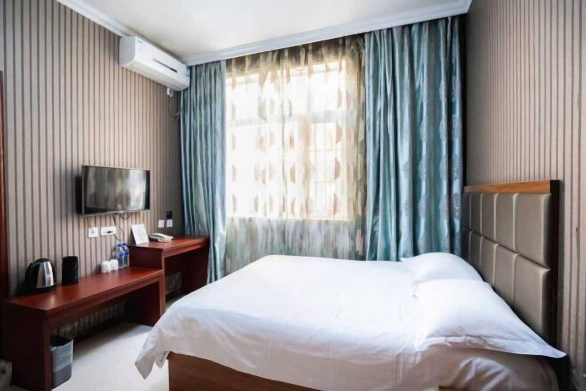 Een hotelkamer met een bed, een bureau met een flatscreen televisie, een koffiezetapparaat en een raam met gordijnen.