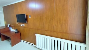 Une pièce avec un mur lambrissé en bois, un téléviseur fixé au mur, un radiateur blanc et un bureau en bois avec une bouilloire.