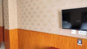 Une pièce avec un papier peint à motifs, un téléviseur à écran plat fixé au mur et un plint en bois.