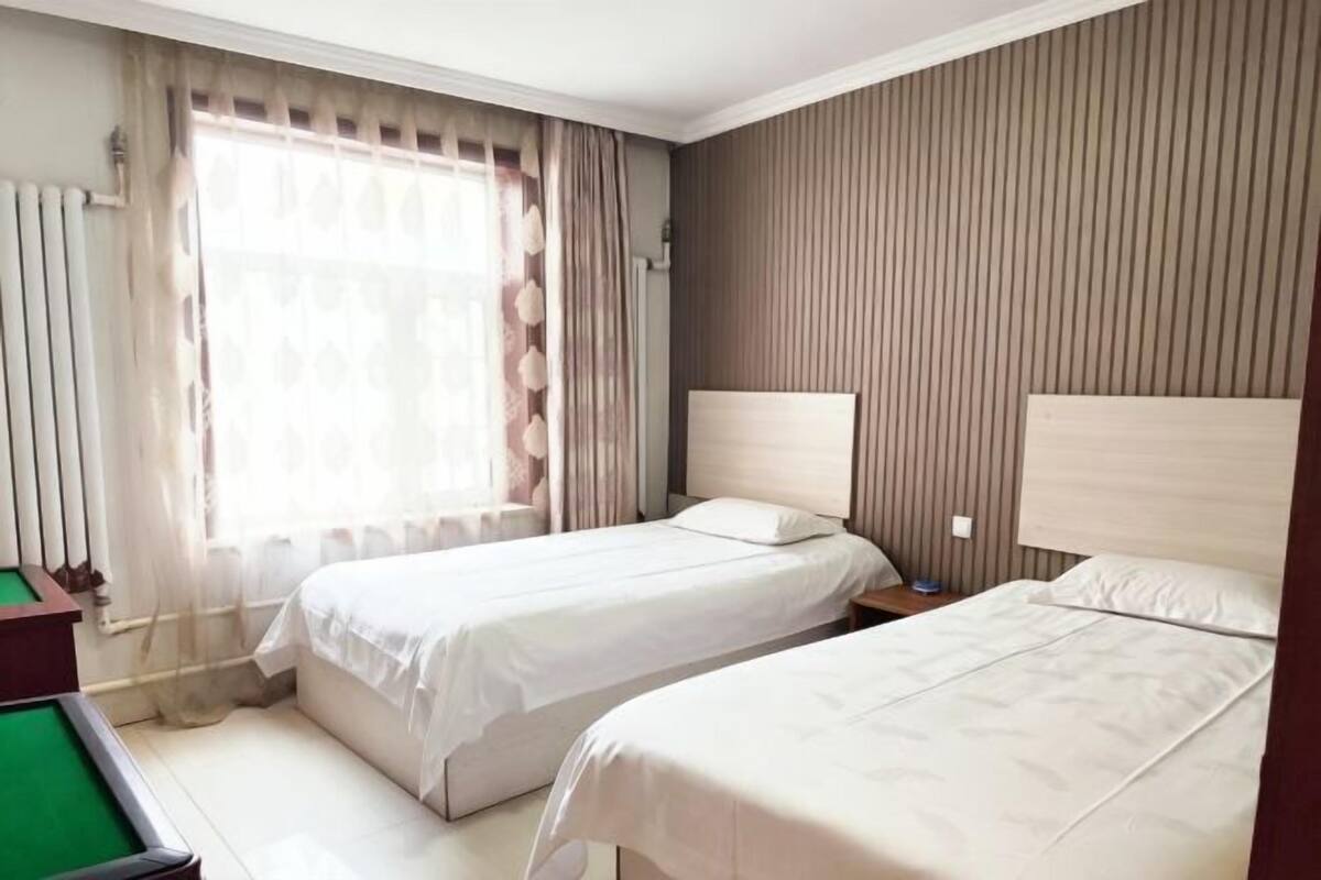 Een hotelkamer met twee bedden, een pooltafel en een groot raam met gordijnen.