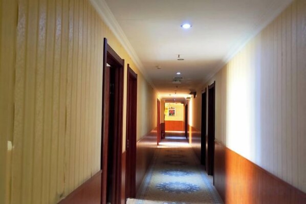 Un couloir d’hôtel avec des portes des deux côtés, une moquette à motifs et un luminaire au plafond.
