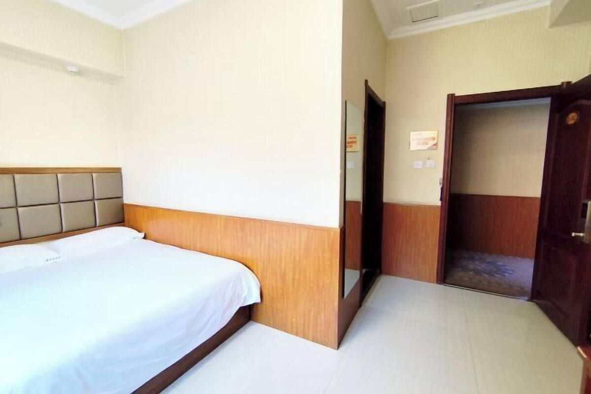 Een hotelkamer met een bed, een houten hoofdbord, een deur en een betegelde vloer.