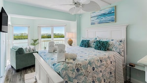 A bedroom with a large bed, a view of the outdoors, a ceiling fan, and a painting on the wall. - Intracoastal-Corner-Pool-Steps to Beach (Indian Shores)