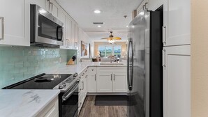 A modern kitchen with white cabinets, a stainless steel refrigerator, a microwave, and a stove. - Intracoastal-Corner-Pool-Steps to Beach (Indian Shores)