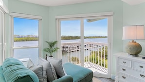 A room with a view of a marina, a balcony with a railing, a sofa with cushions, a lamp, and a white dresser. - Intracoastal-Corner-Pool-Steps to Beach (Indian Shores)