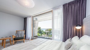 Une chambre d’hôtel moderne avec un grand lit, une chaise en bois, une petite table et un balcon avec vue.