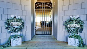 A wooden entrance with a metal gate, flanked by two 'HELLO' signs and greenery. - Starfish Wishes: Beachfront Duplex Unit, Great location, remodeled, Pet Friendly (St. George Island)