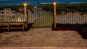 A paved pathway leading to a beach with a gated entrance, a bench, and a pool area. - Starfish Wishes: Beachfront Duplex Unit, Great location, remodeled, Pet Friendly (St. George Island)