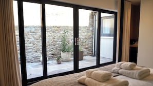 A hotel room with a large sliding glass door leading to a stone-walled courtyard with potted plants. - Wilding Hotel (Kirkby Stephen)
