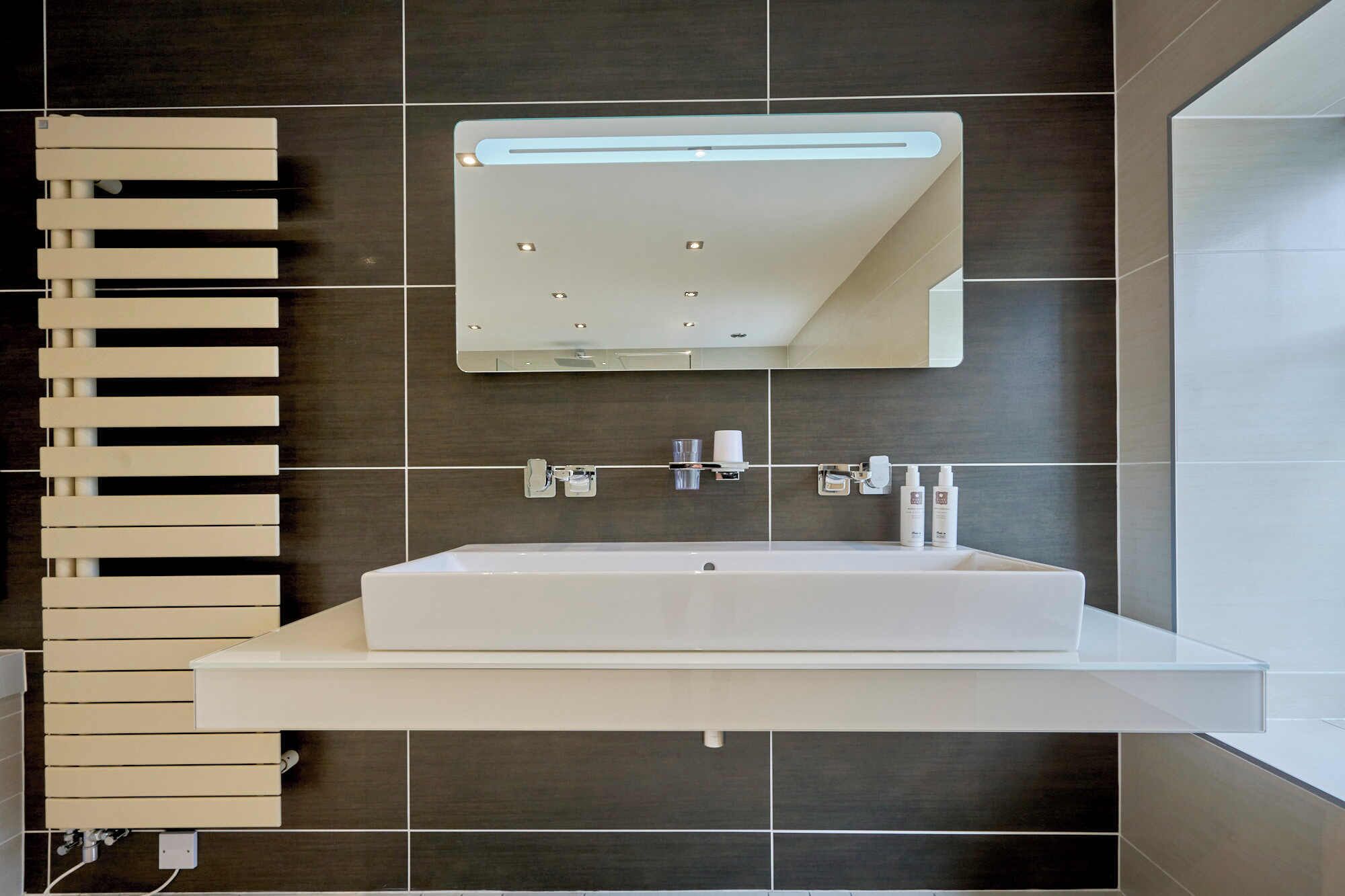 A modern bathroom with a large rectangular sink, a mirror above it, and a towel rack to the left.