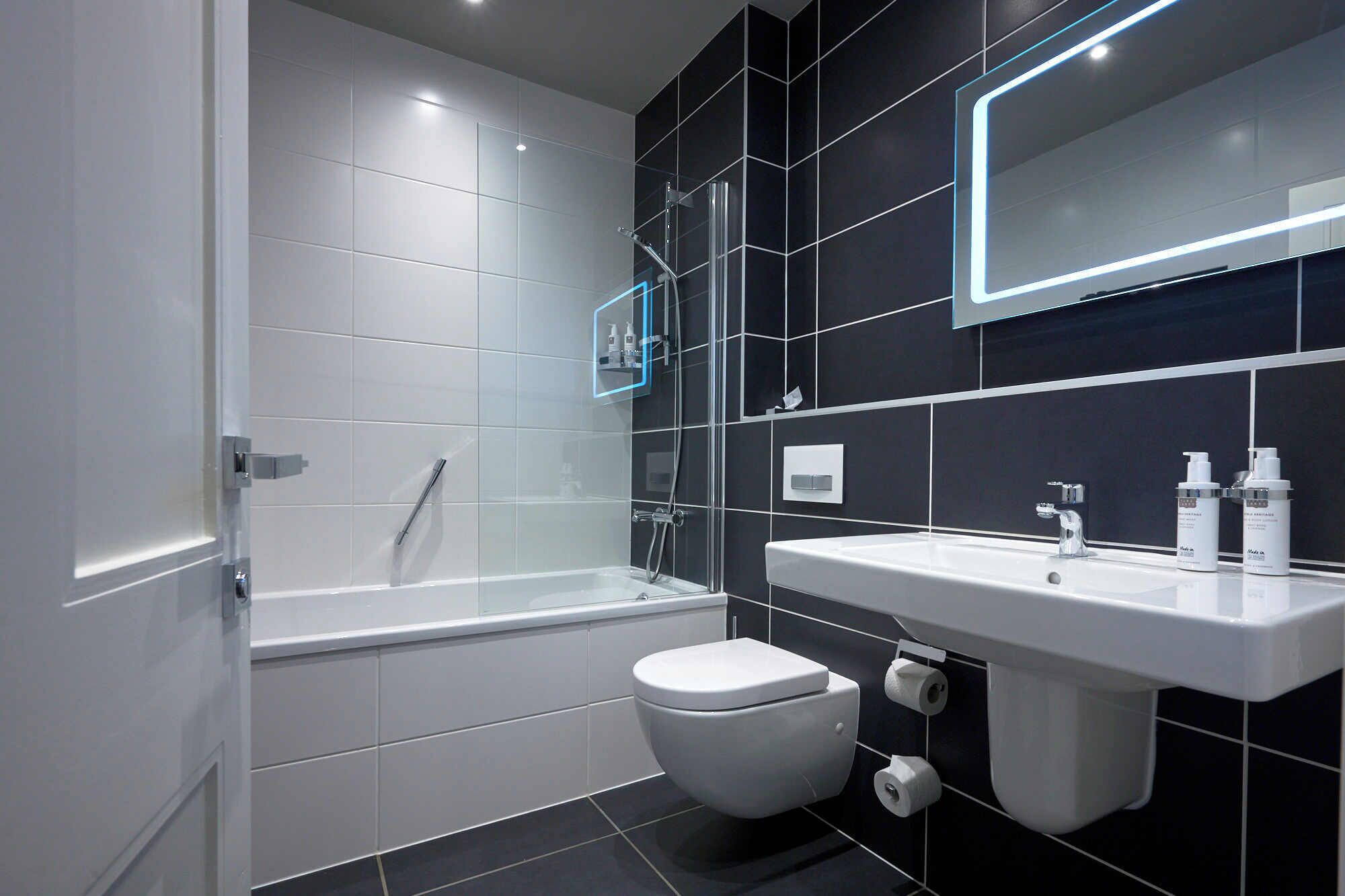 A modern bathroom with a bathtub, toilet, and sink, featuring black and white tiles and a glass shower enclosure.