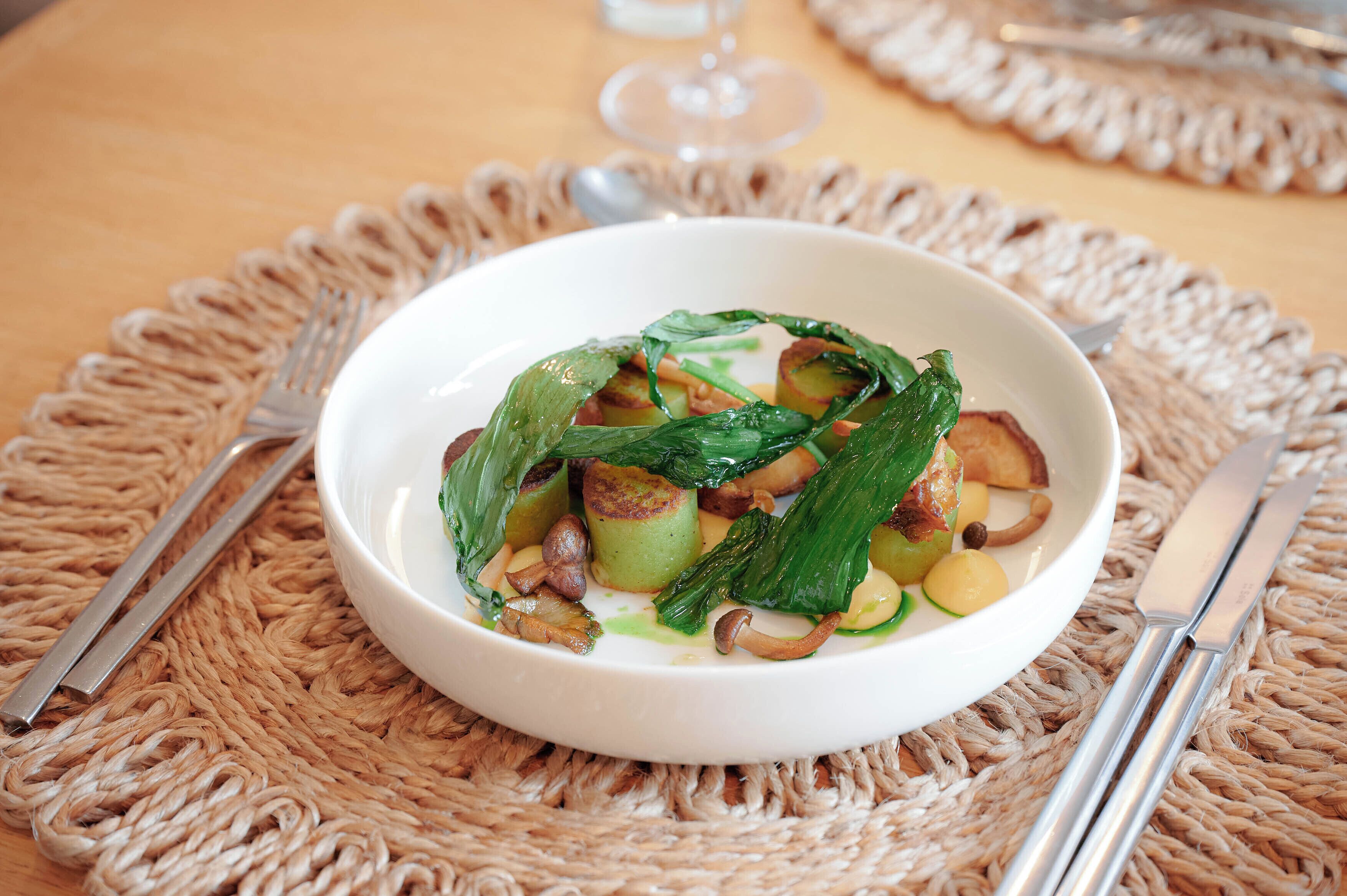 A white bowl of food on a woven placemat with a fork and knife beside it.